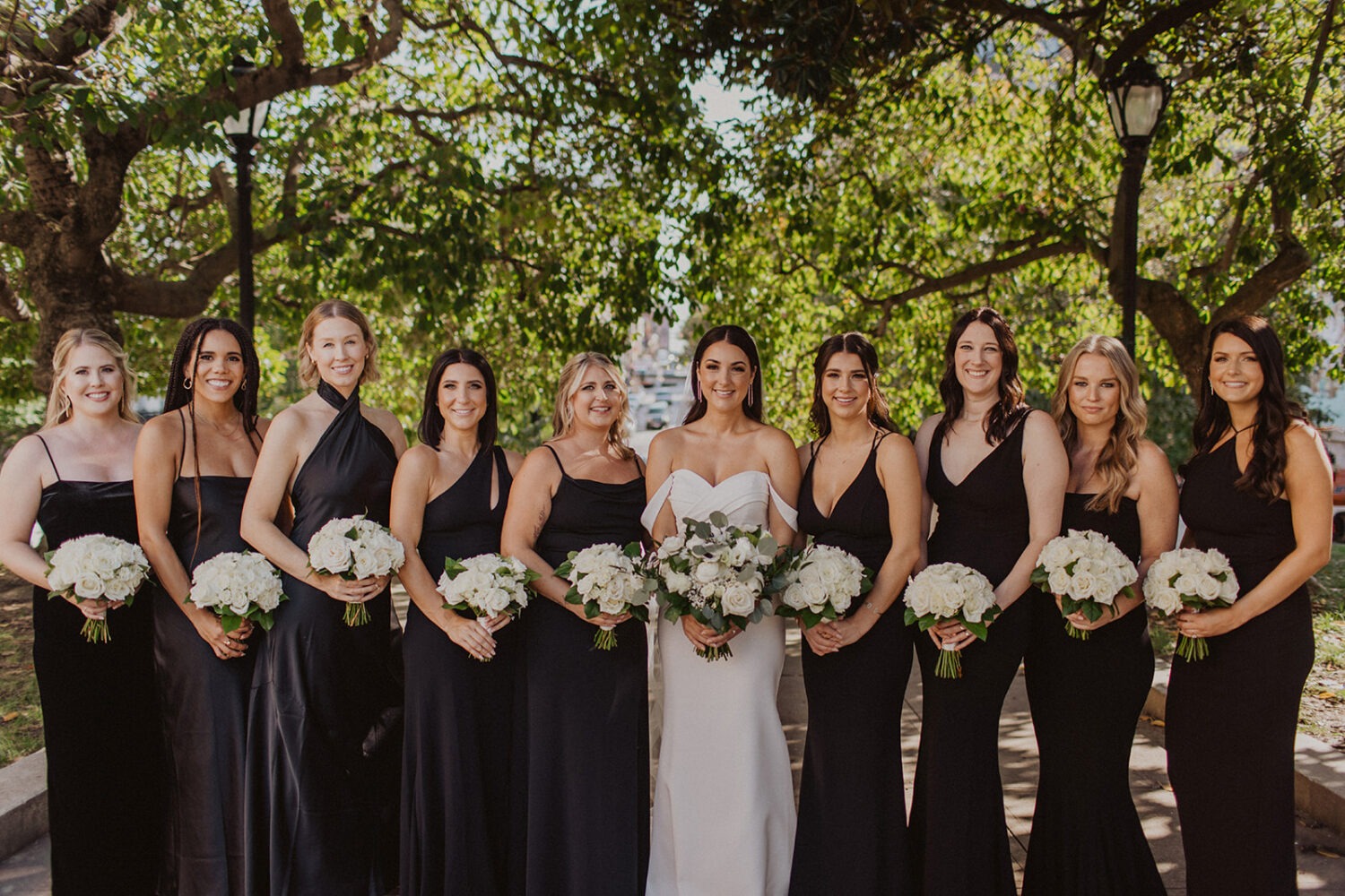 bridesmaids stand with bride holding bouquets under trees