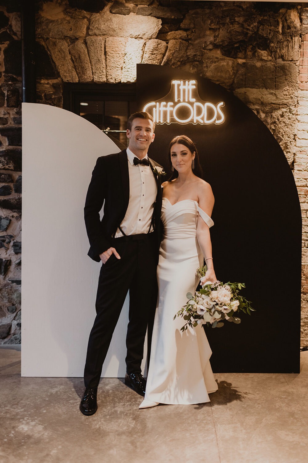 couple stands in front of neon name sign at Mt. Washington Mill Dye House wedding venue