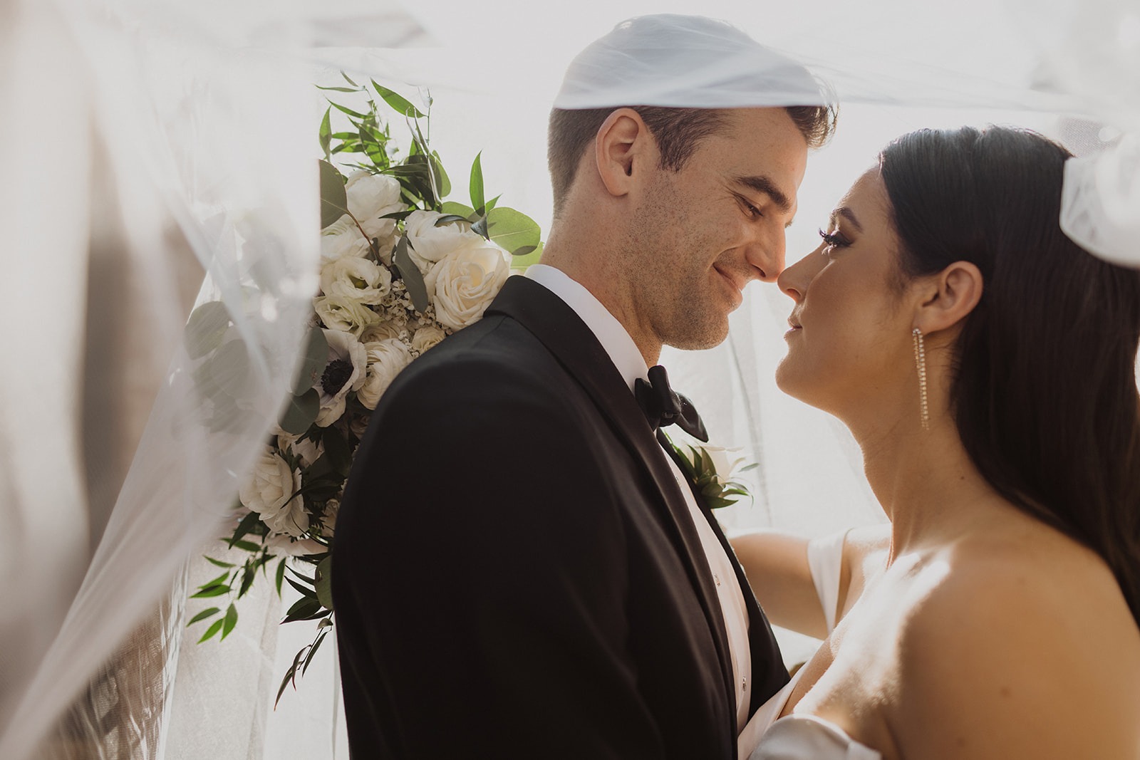 couple kisses under wedding veil with wedding bouquet