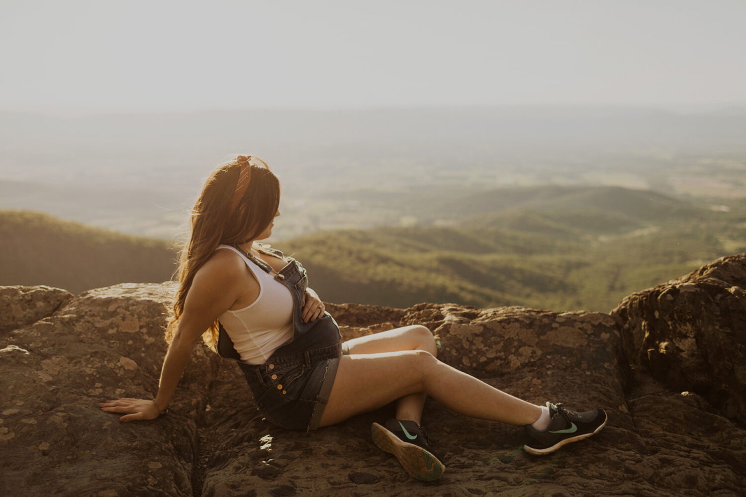 mom sits on mountaintop while embracing pregnant belly at maternity session