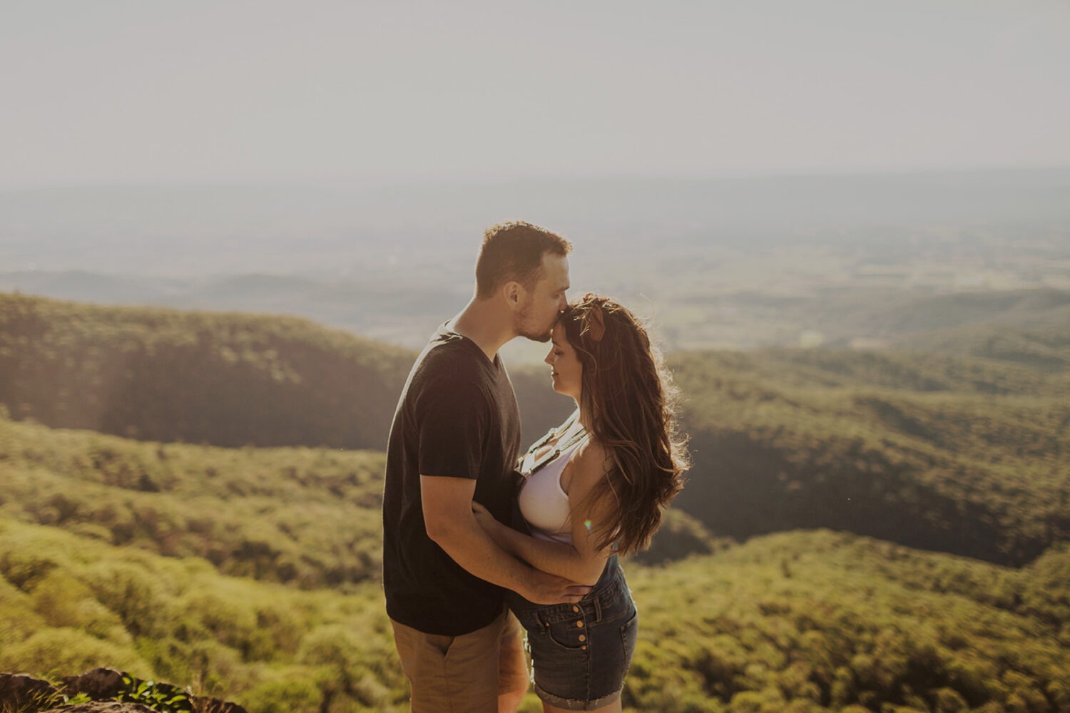 Husband kisses wife's forehead for couples adventure on top of mountain 