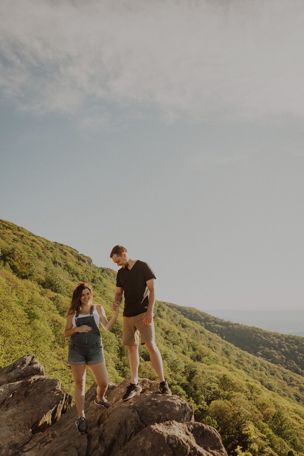 couple walks holding hands on mountaintop at sunset maternity session 