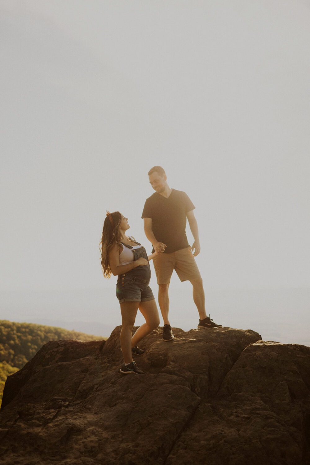 couple walks holding hands on mountaintop at sunset maternity session 