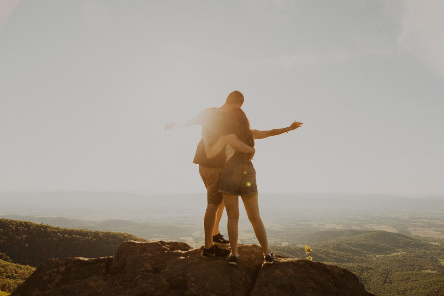 couple embraces standing on top of mountain at sunset couples adventure