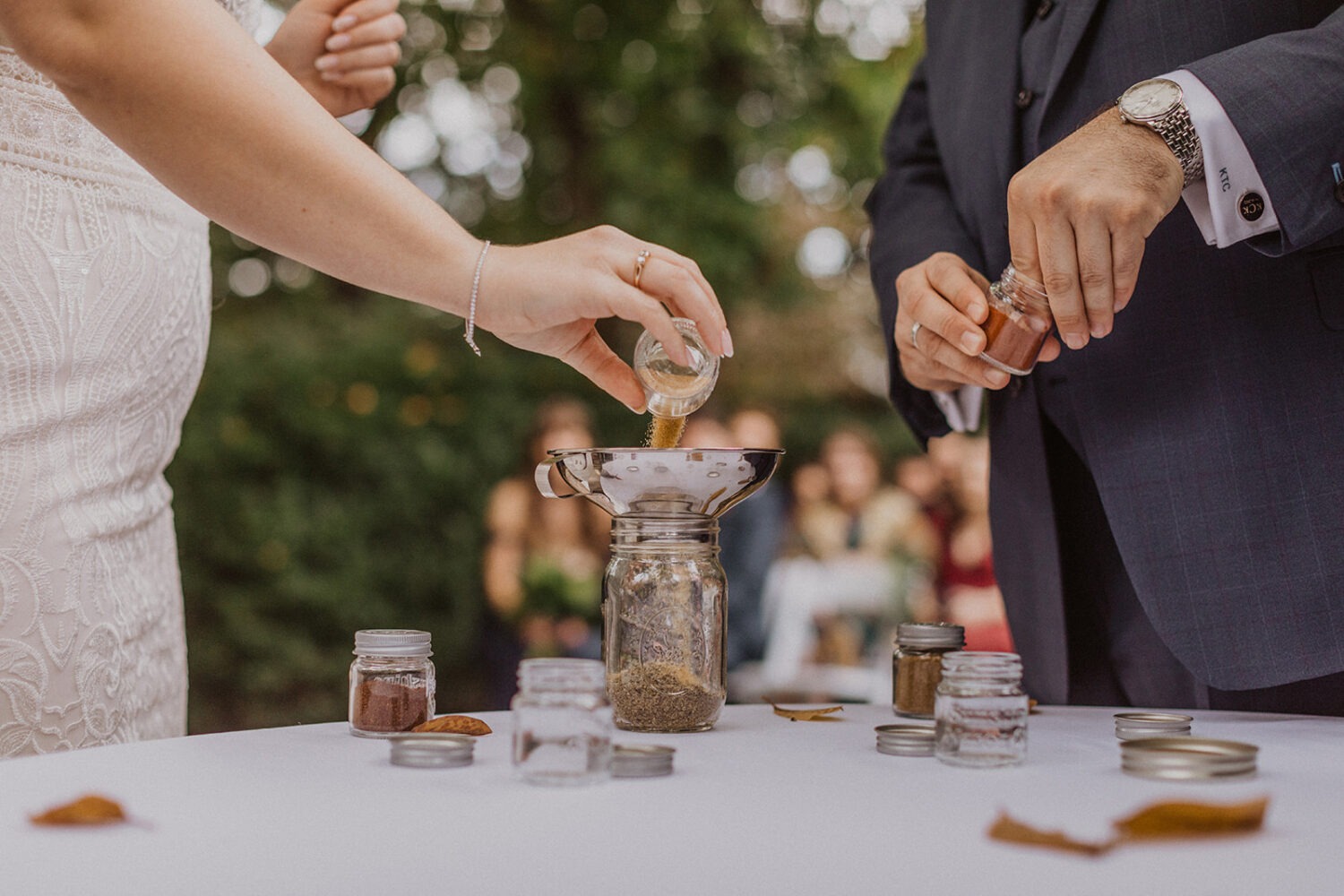 couple pours spices into mason jar at outdoor wedding 