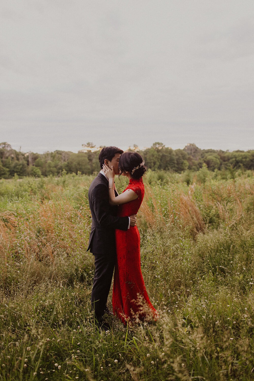 couple kisses while standing in meadow with high grass