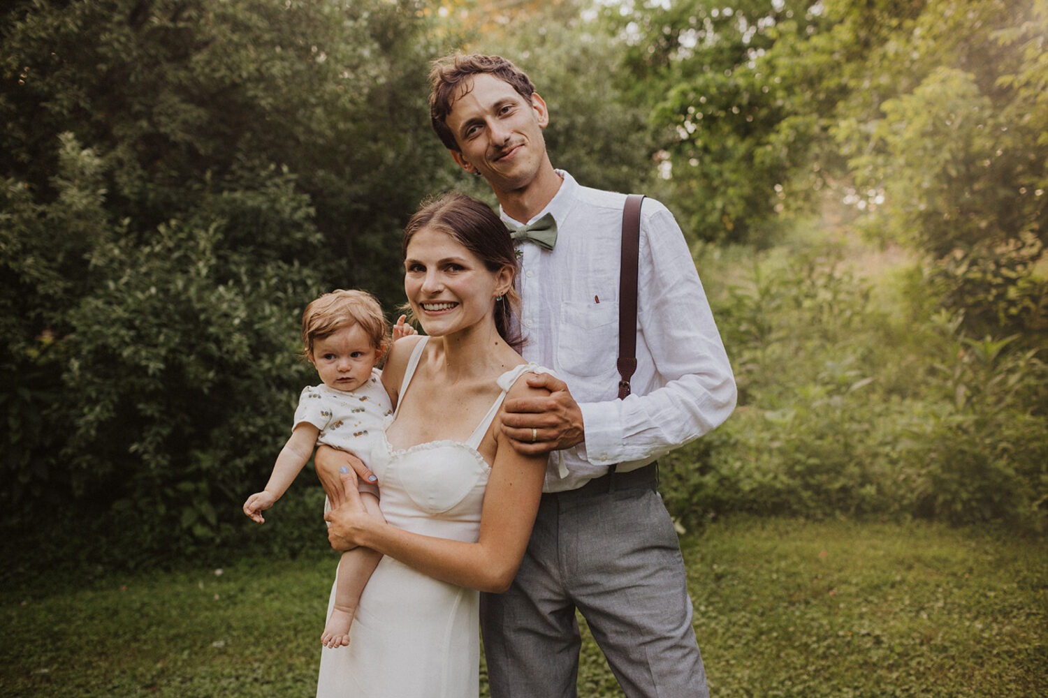 couple holds baby together at outdoor wedding