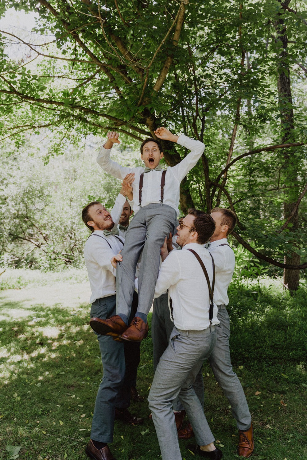 groomsmen throw groom up into the air pulling from barn wedding ideas 