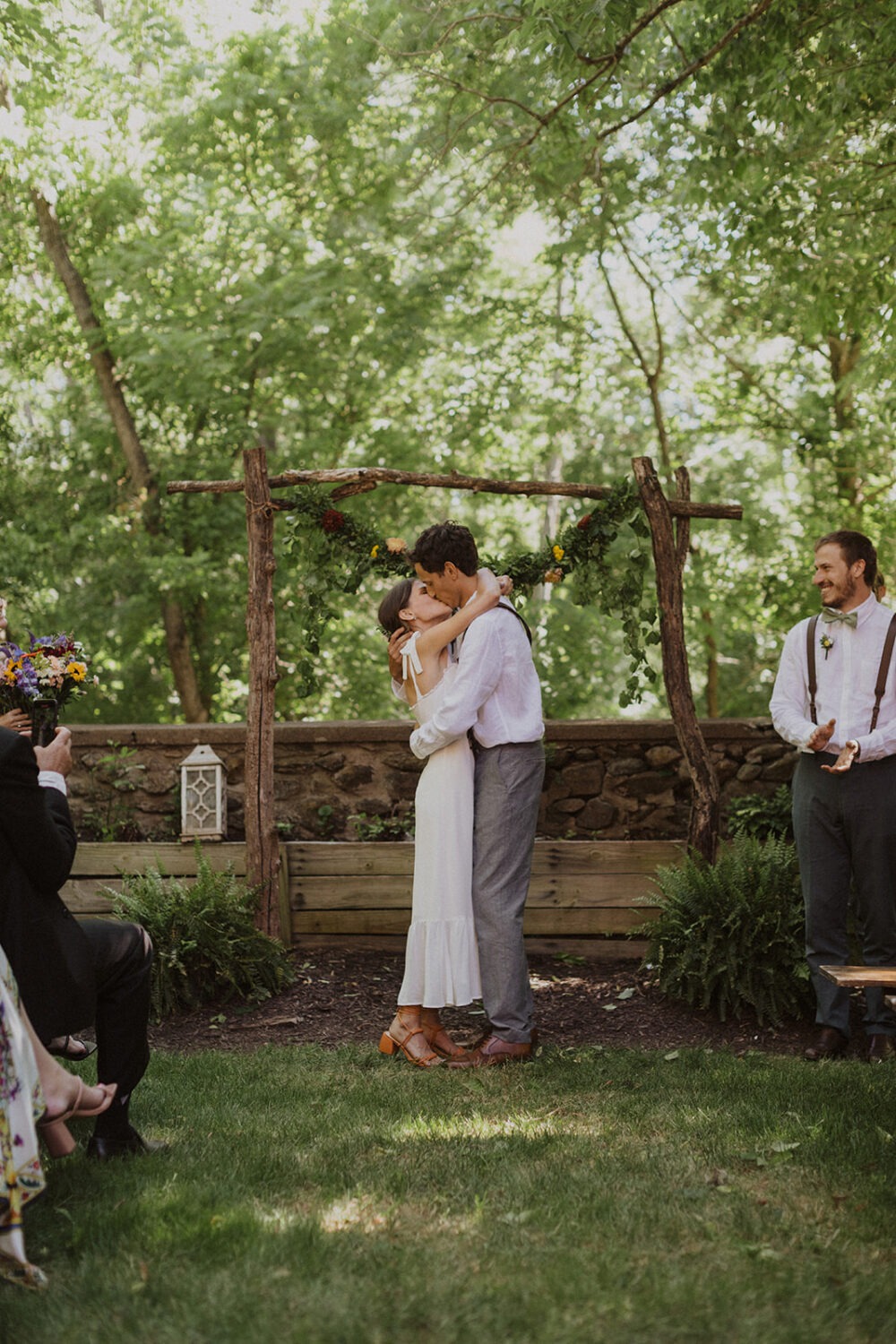 couple kisses under floral wedding arch at rustic outdoor wedding venue 