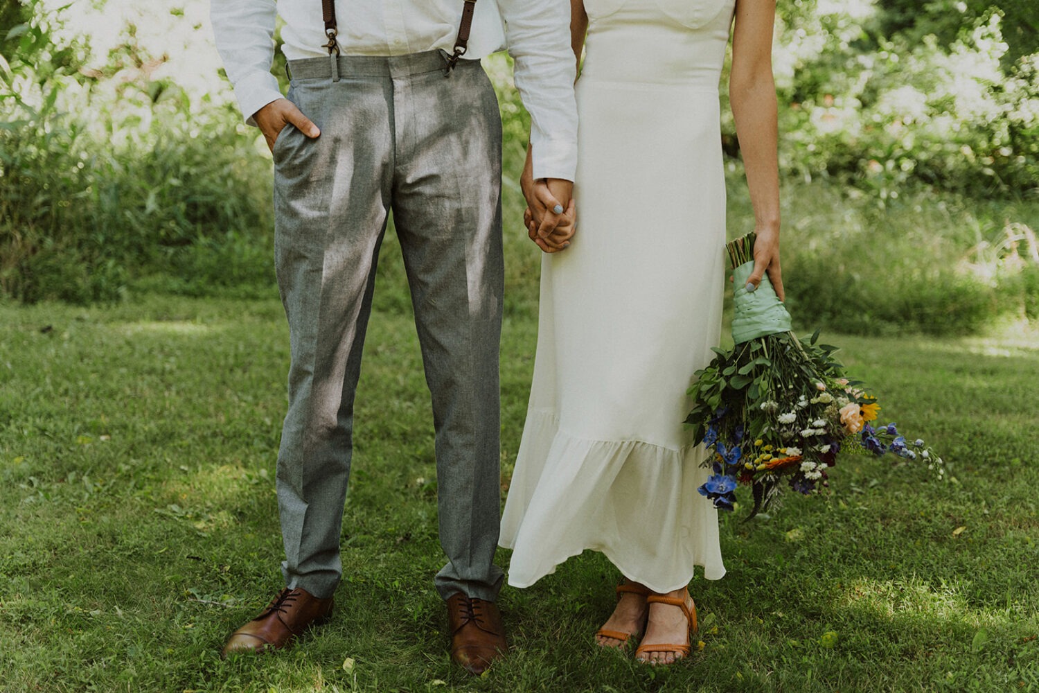 couple holds hands with wedding bouquet at rustic outdoor wedding 