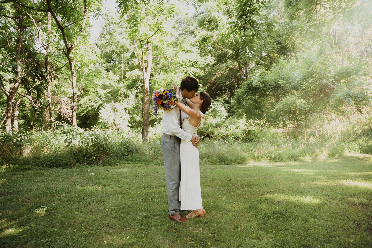 couple kisses at outdoor wedding under trees