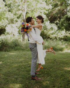 groom lifts bride while holding wedding bouquet at outdoor wedding
