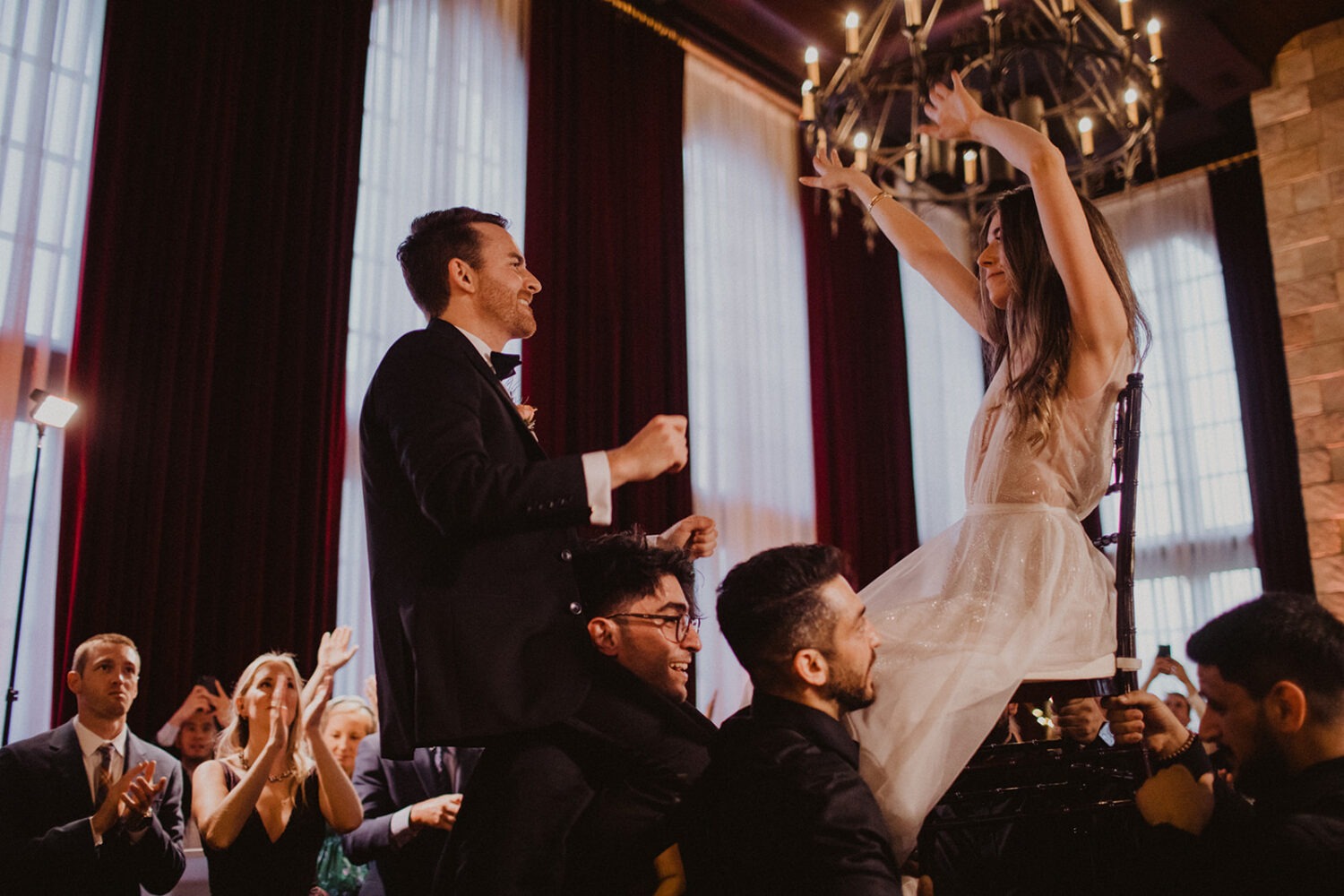 couple dances while lifted up on shoulders and chairs at wedding reception 