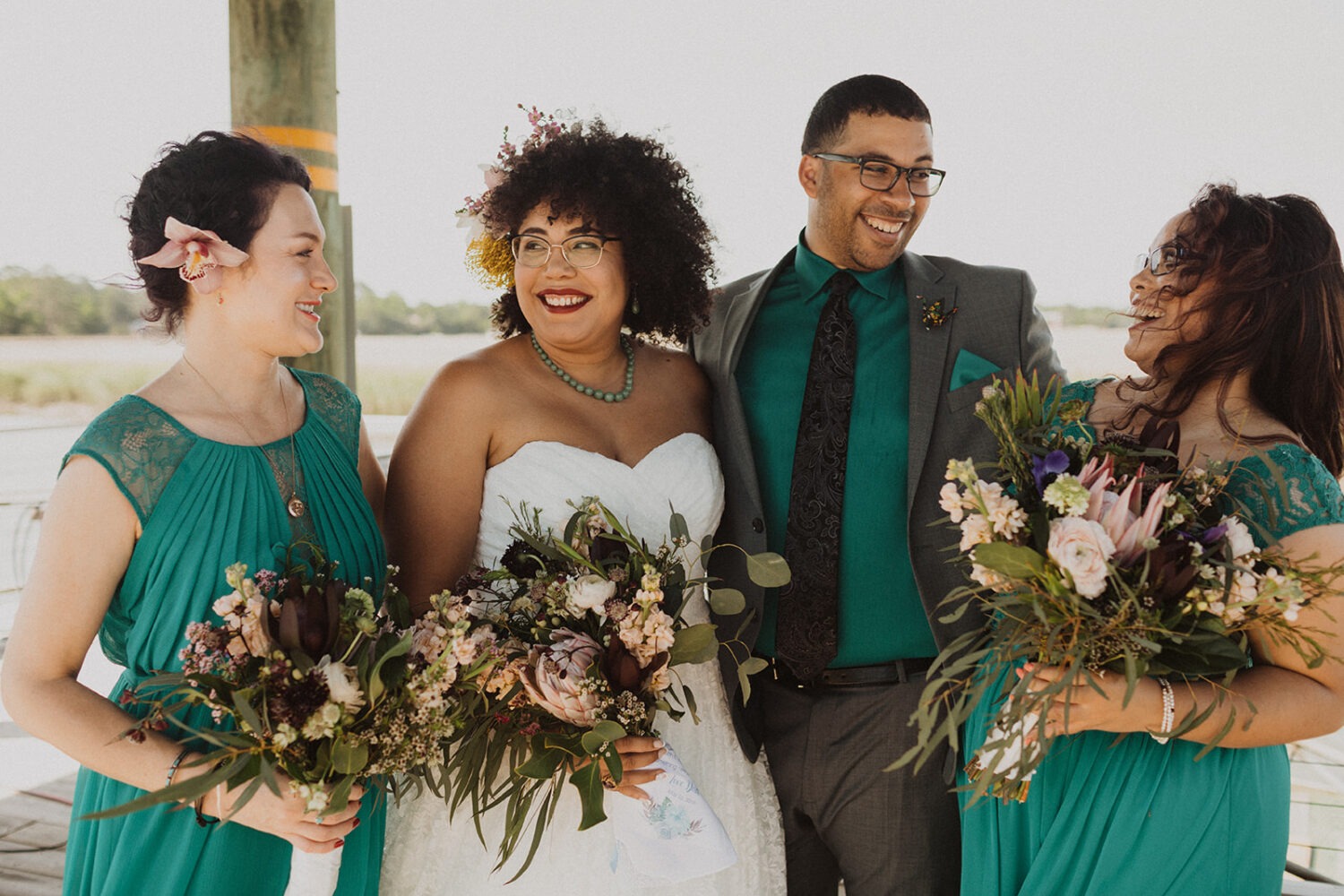 bride laughs with wedding party holding tropical flower bouquets