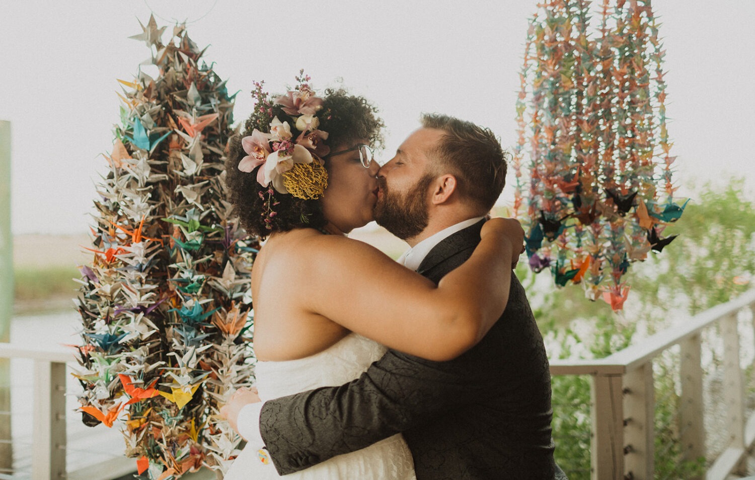 couple kisses surrounded by hanging paper cranes at summer wedding