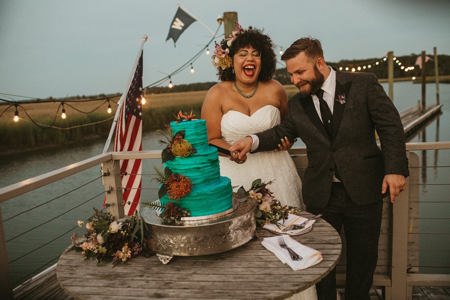 couple cuts blue tropical flower wedding cake at summer wedding