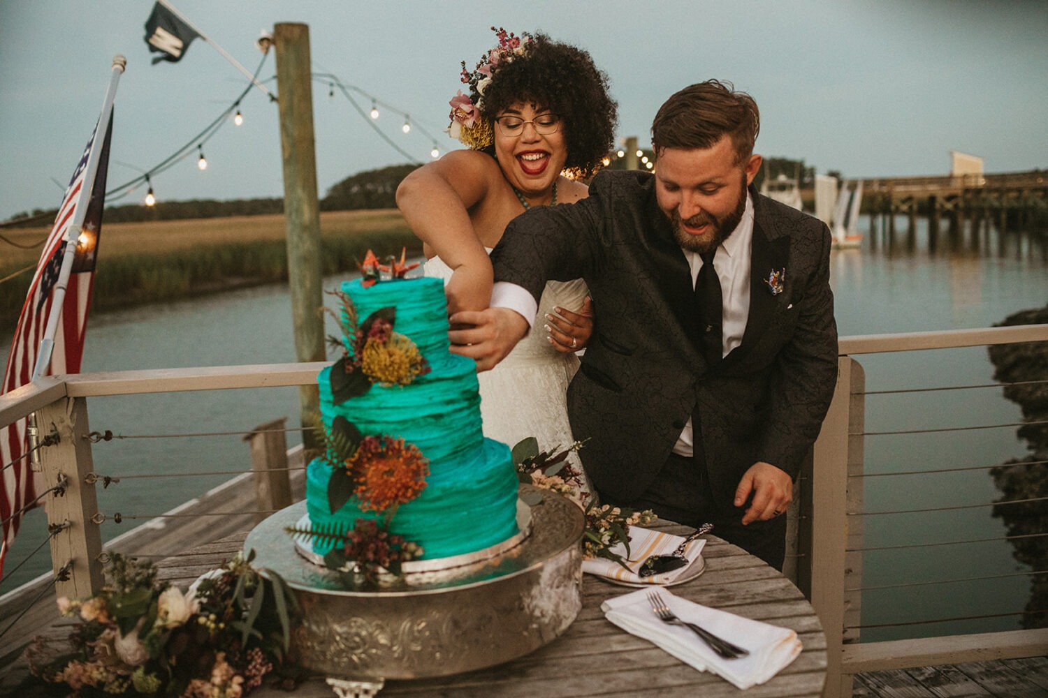 couple cuts blue tropical flower wedding cake at summer wedding