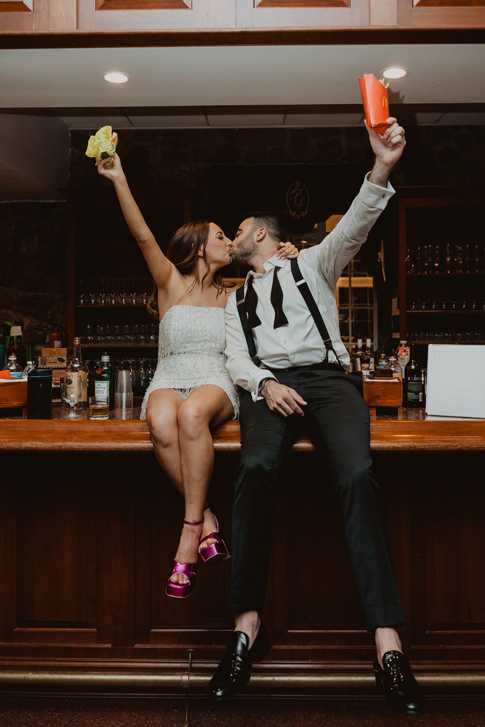 couple cheers with food sitting on bar at wedding reception