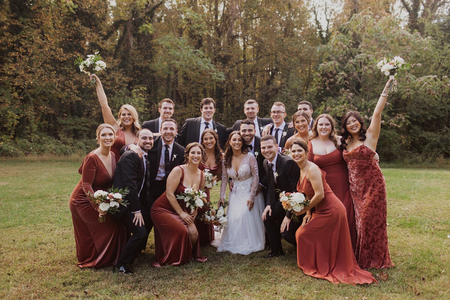 couple poses surrounded by wedding party at outdoor wedding