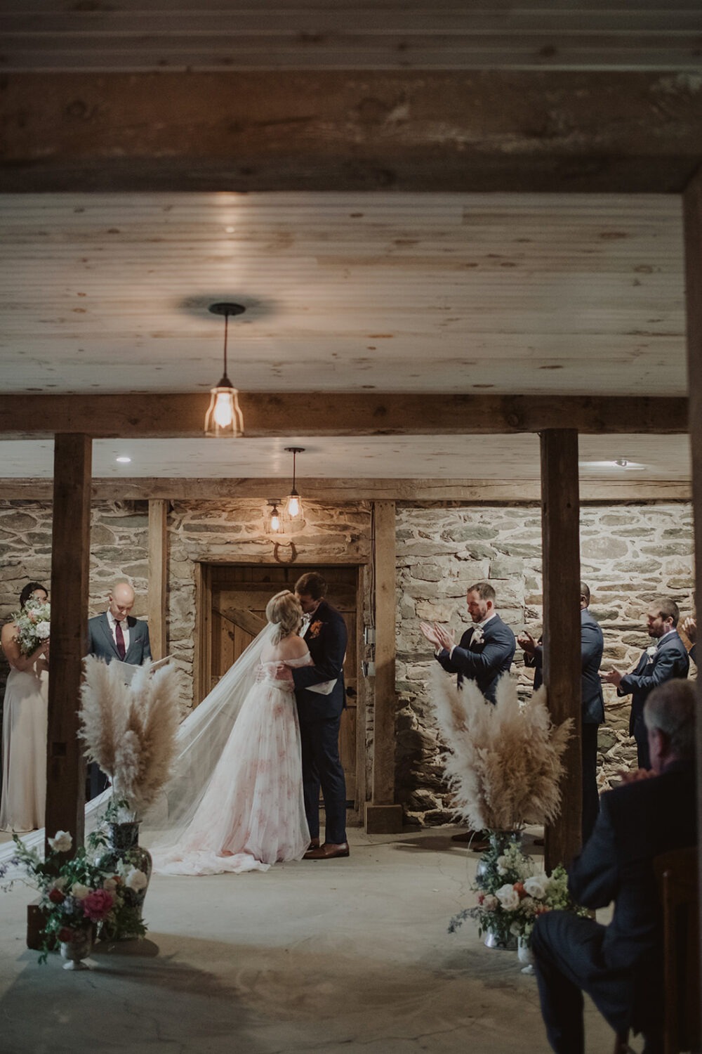 couple kisses during wedding ceremony inside wedding barn