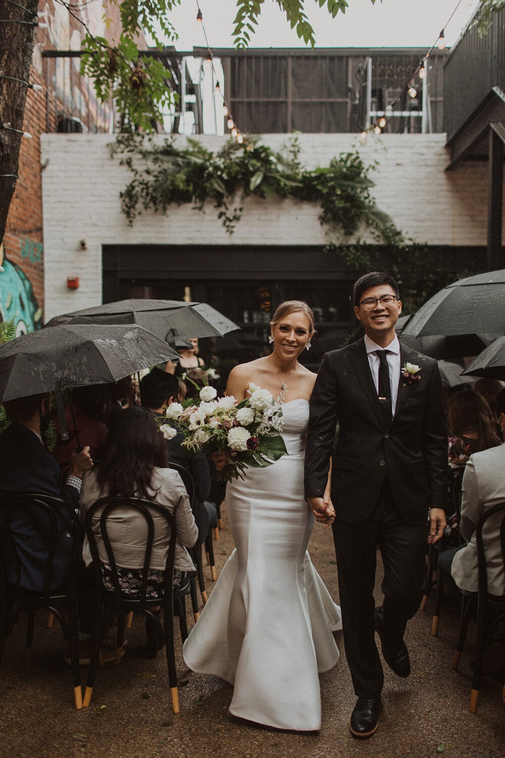 couple exits rainy wedding ceremony holding hands