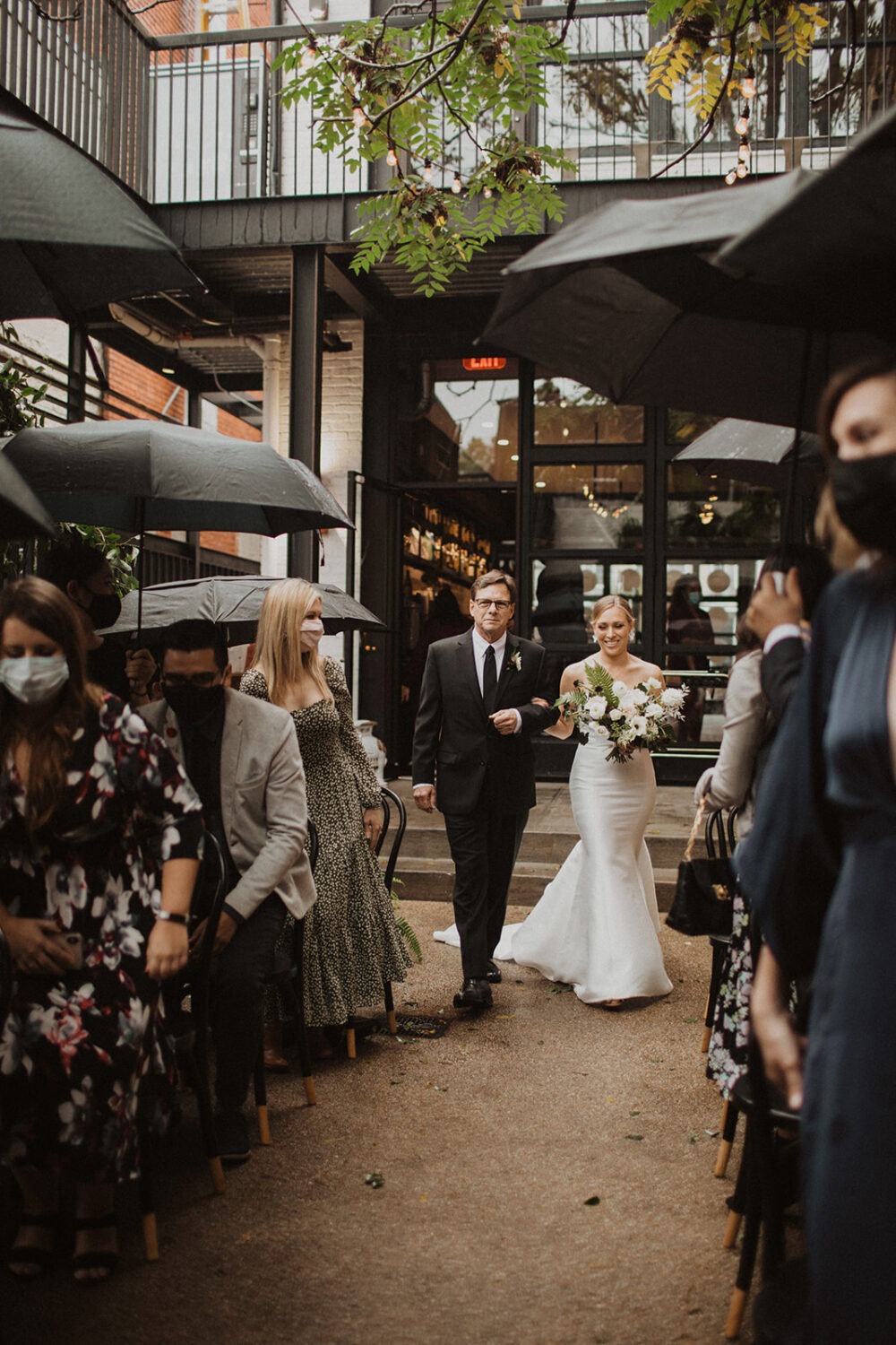 bride walks down aisle at outdoor rainy wedding ceremony