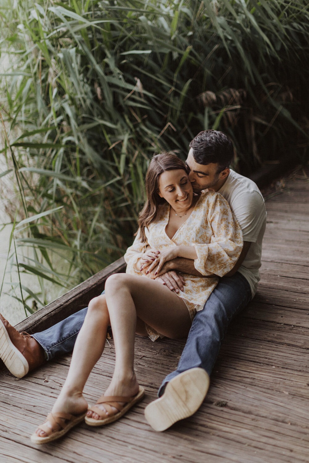 couple walks along boardwalk under trees at engagement session