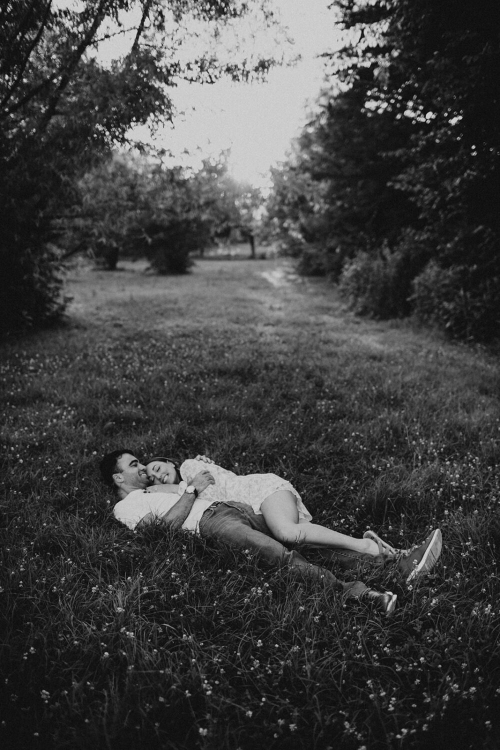 couple holds each other lying in grass at summer engagement photos