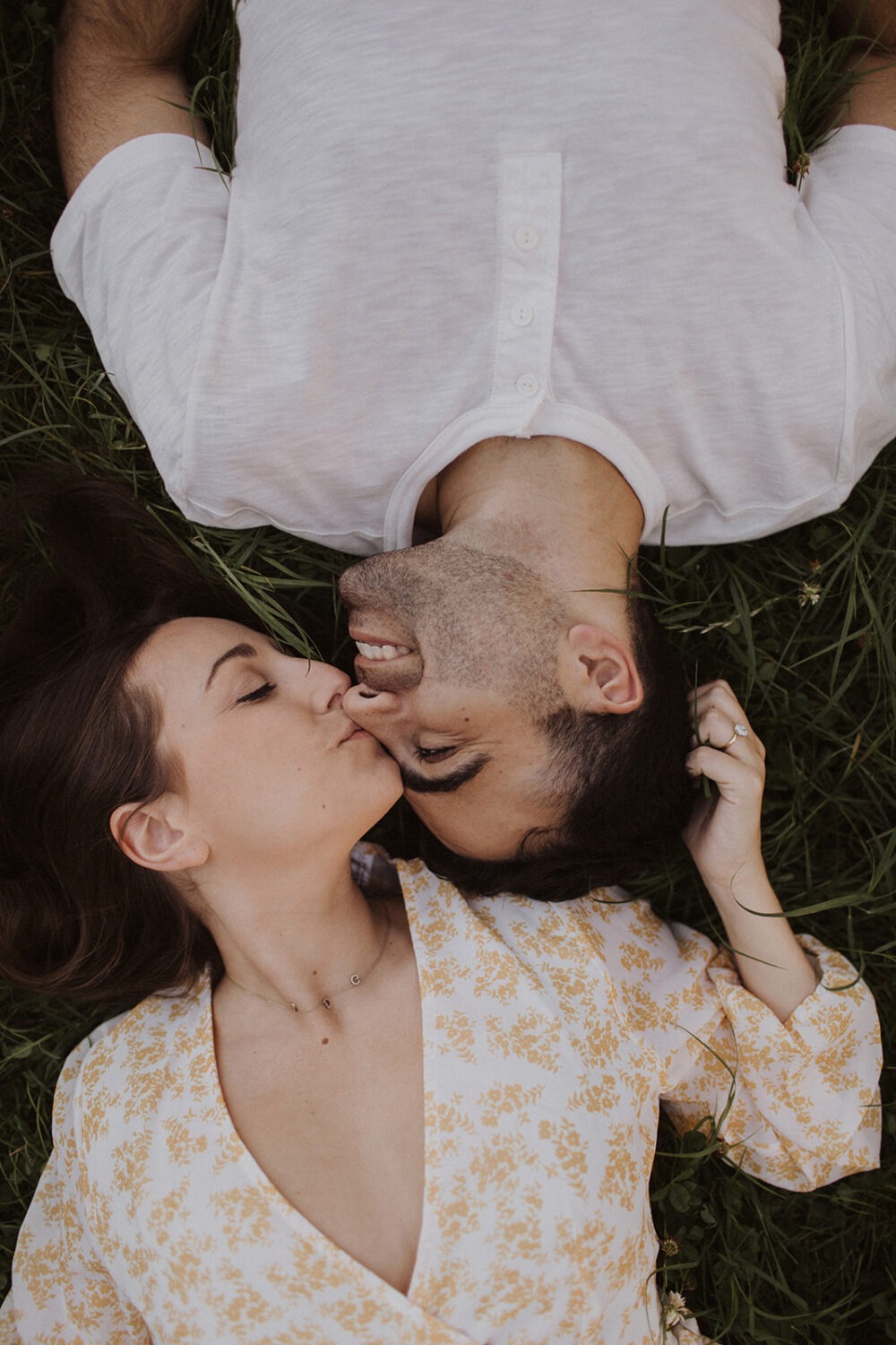 couple holds each other lying in grass at summer engagement photos