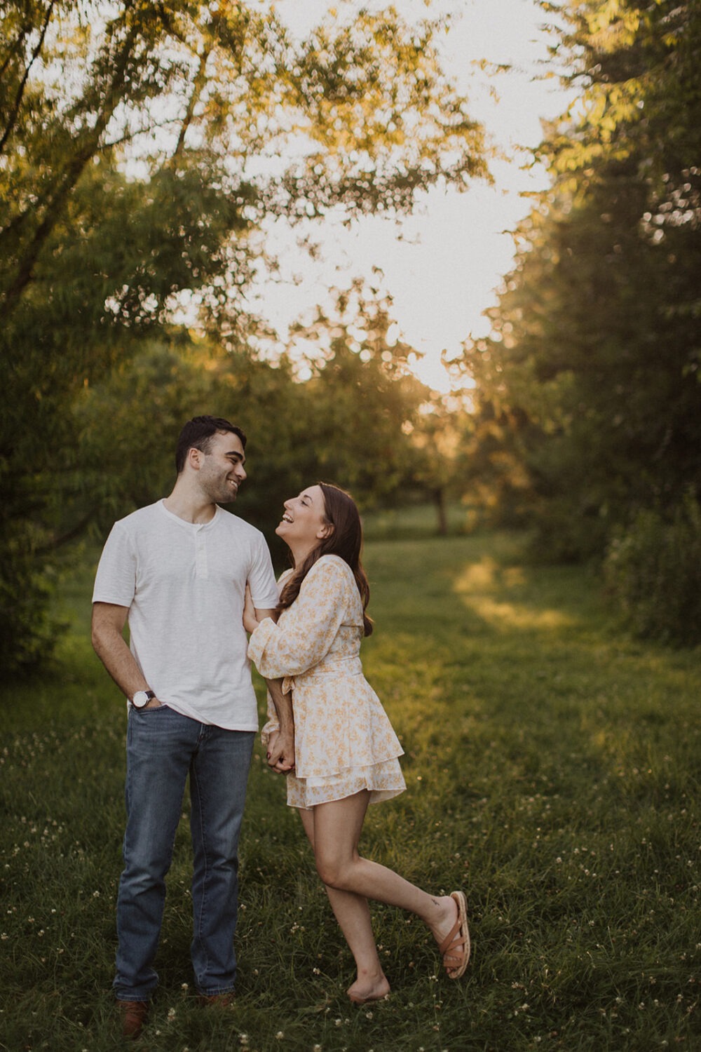 couple stands in grassy field at sunset under trees