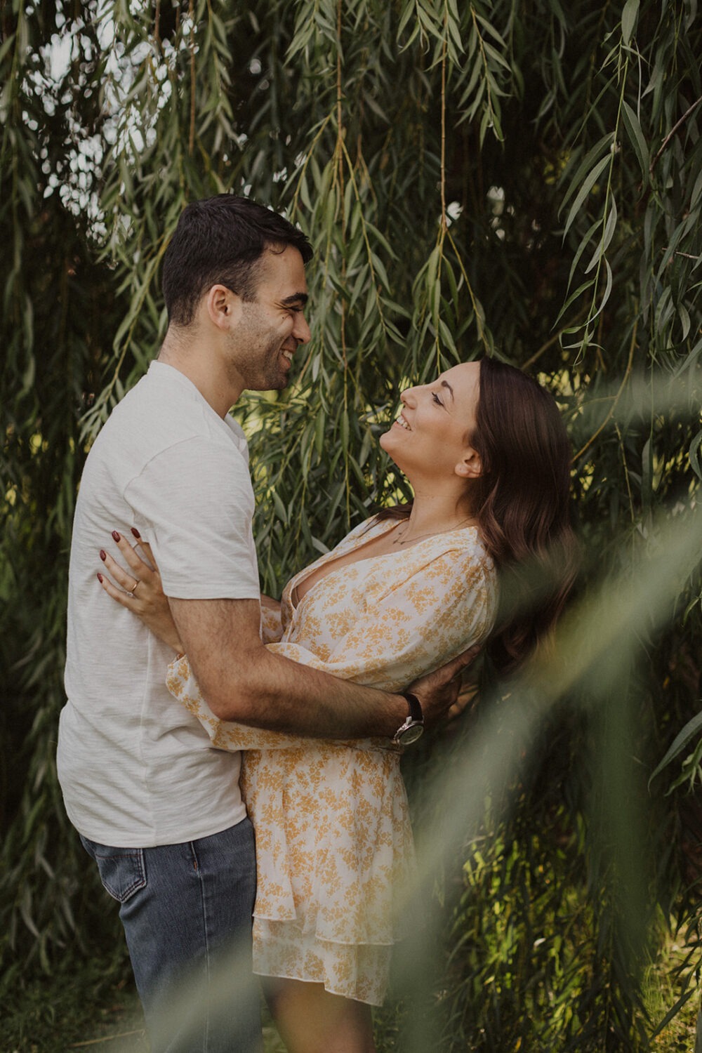couple embraces under trees during summer engagement photos