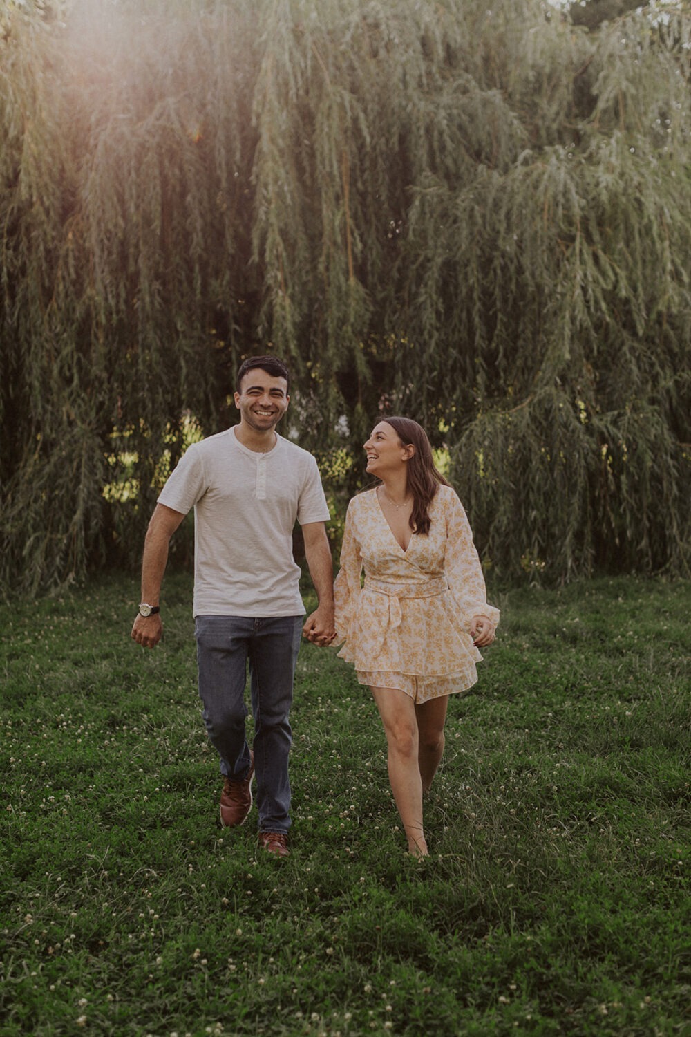 couple walks under trees during summer engagement photos
