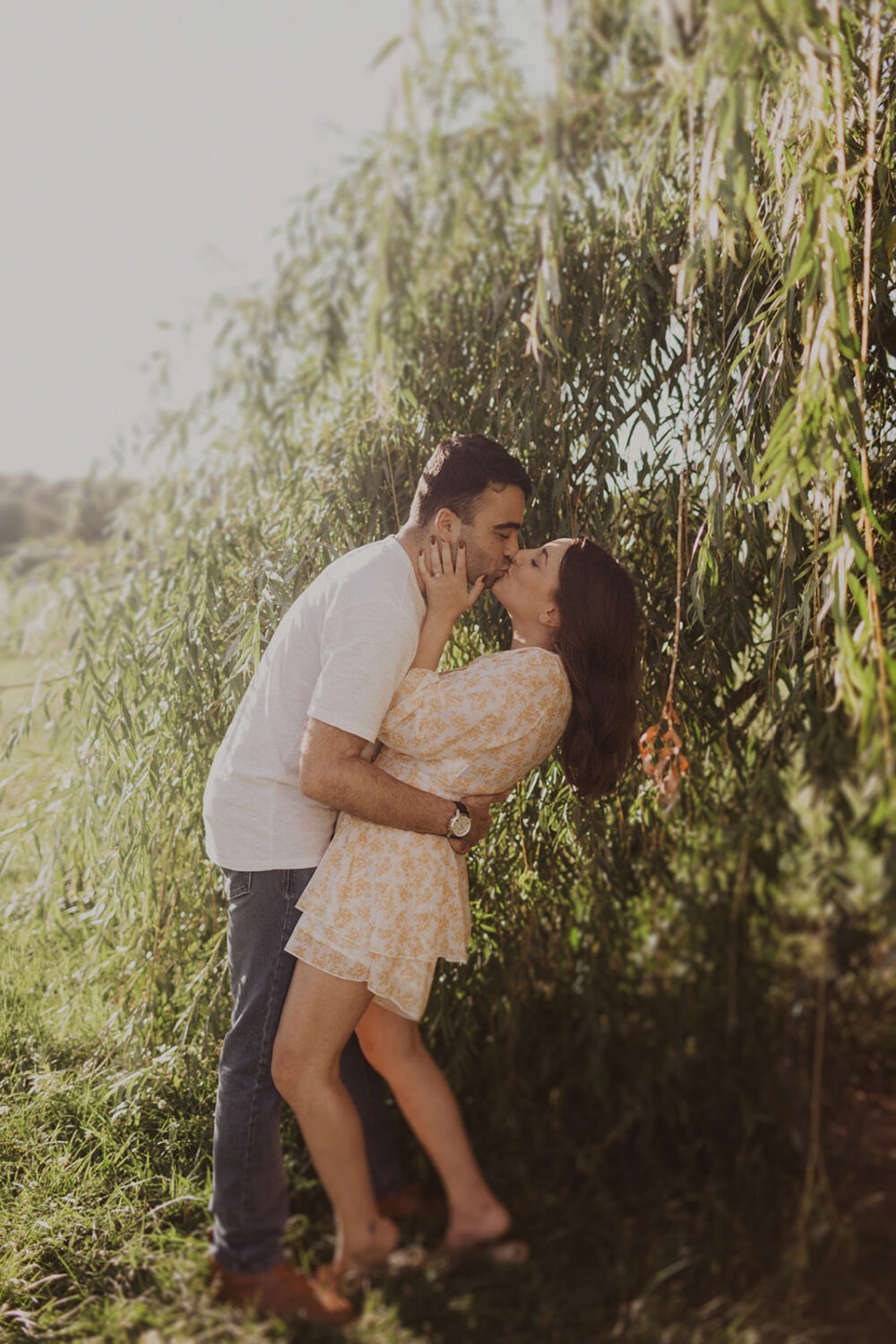 couple kisses underneath tree during summer engagement photos