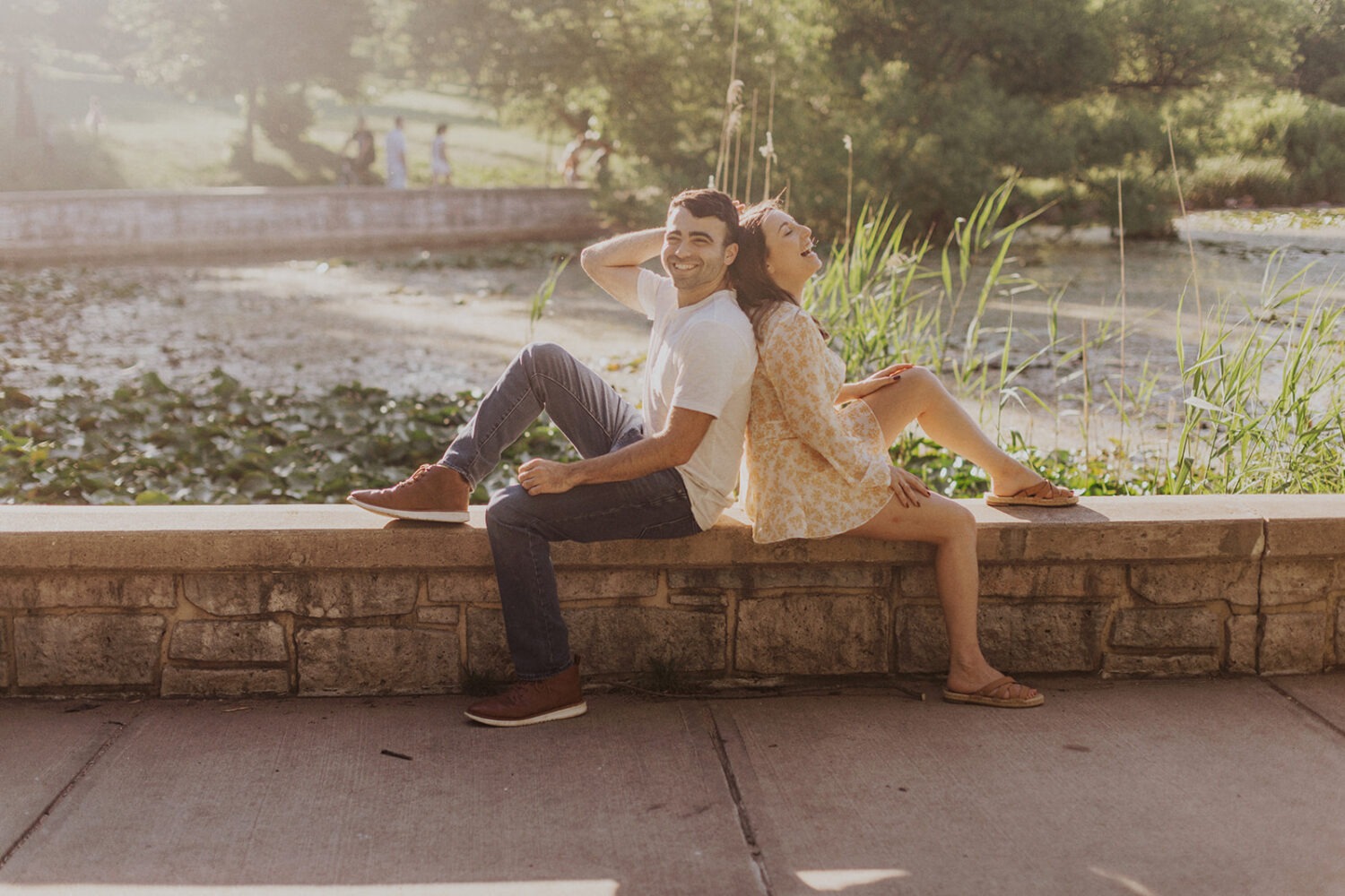 couple sits alongside pond capturing summer engagement photos