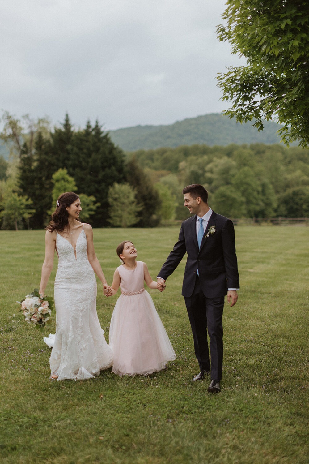 couple walks holding hands with flower girl at backyard wedding 