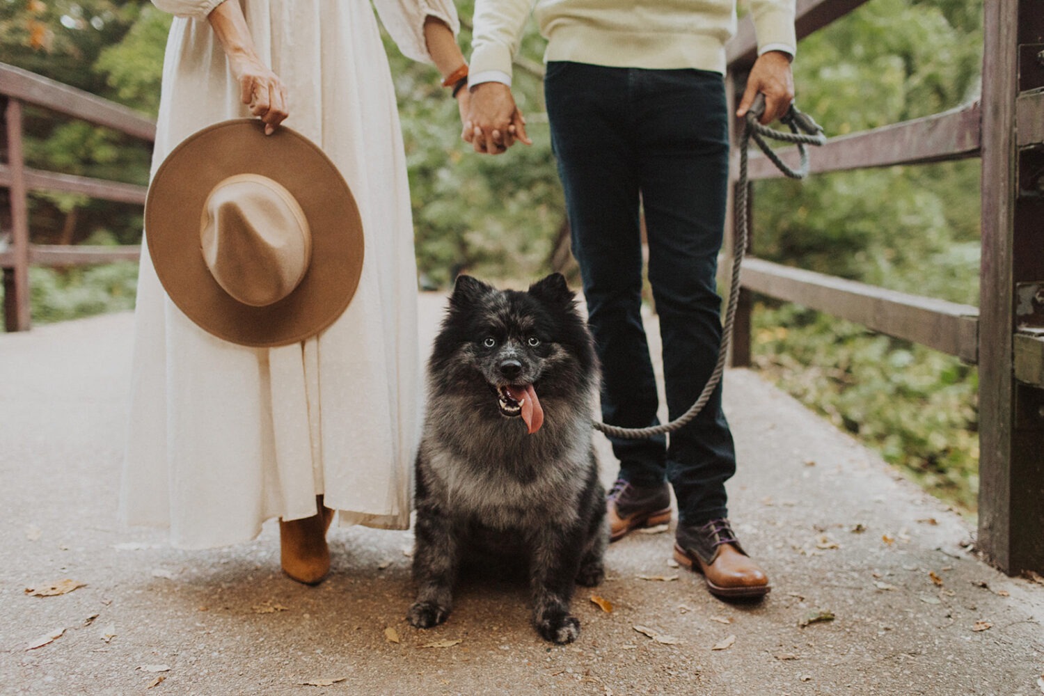 couple poses with dog wearing engagement shoot outfit with hat