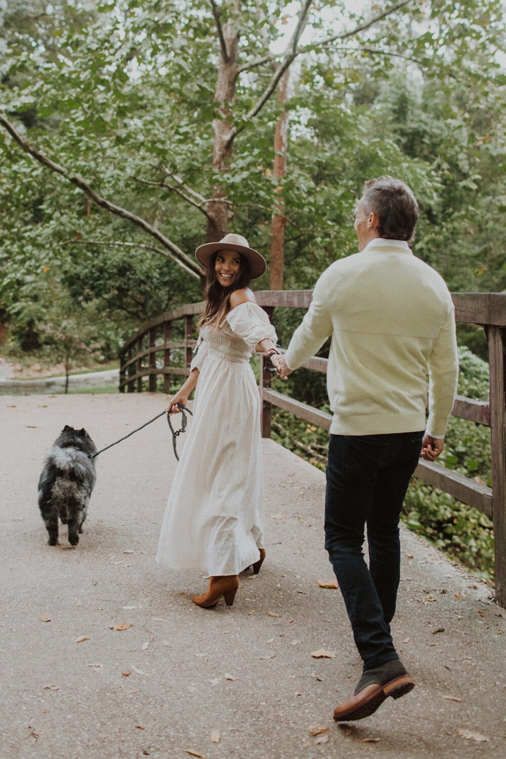 couple walks holding hands wearing white engagement shoot outfit