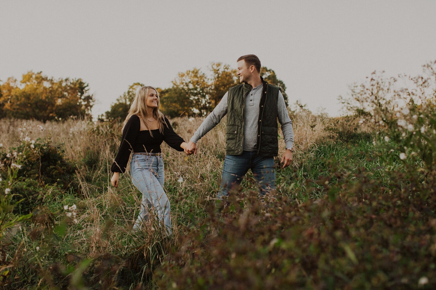couple walks holding hands wearing engagement shoot outfits 