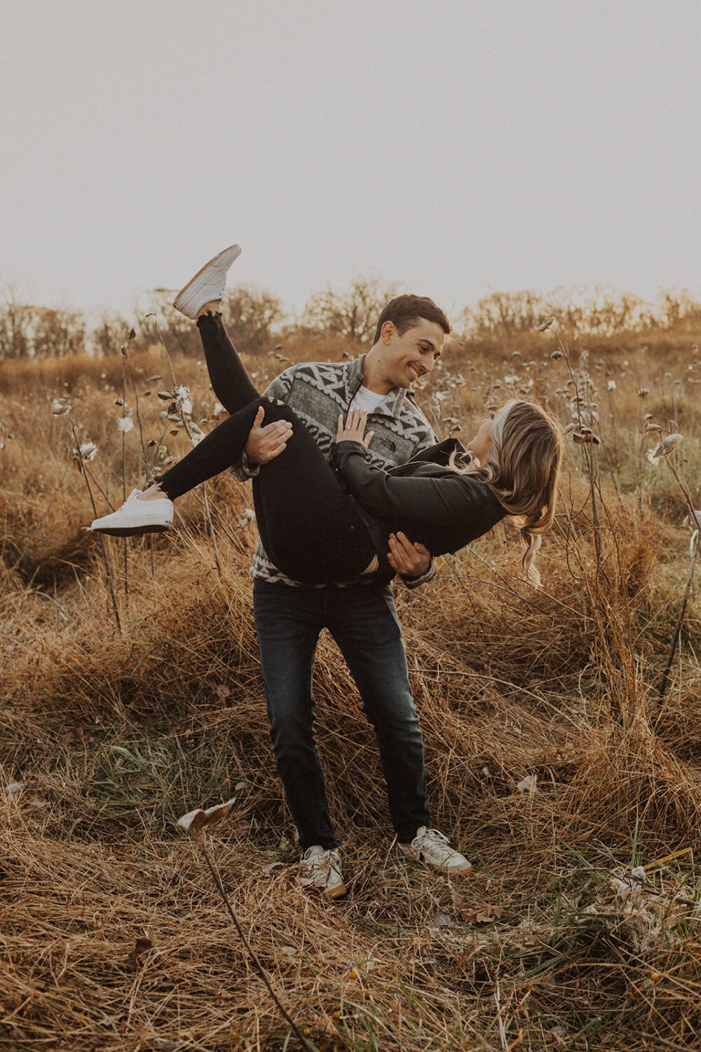 groom holds bride in field at engagement session