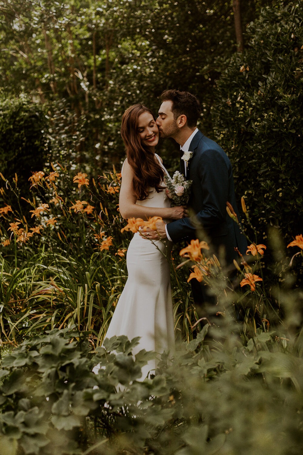 couple kisses in flowers at backyard wedding