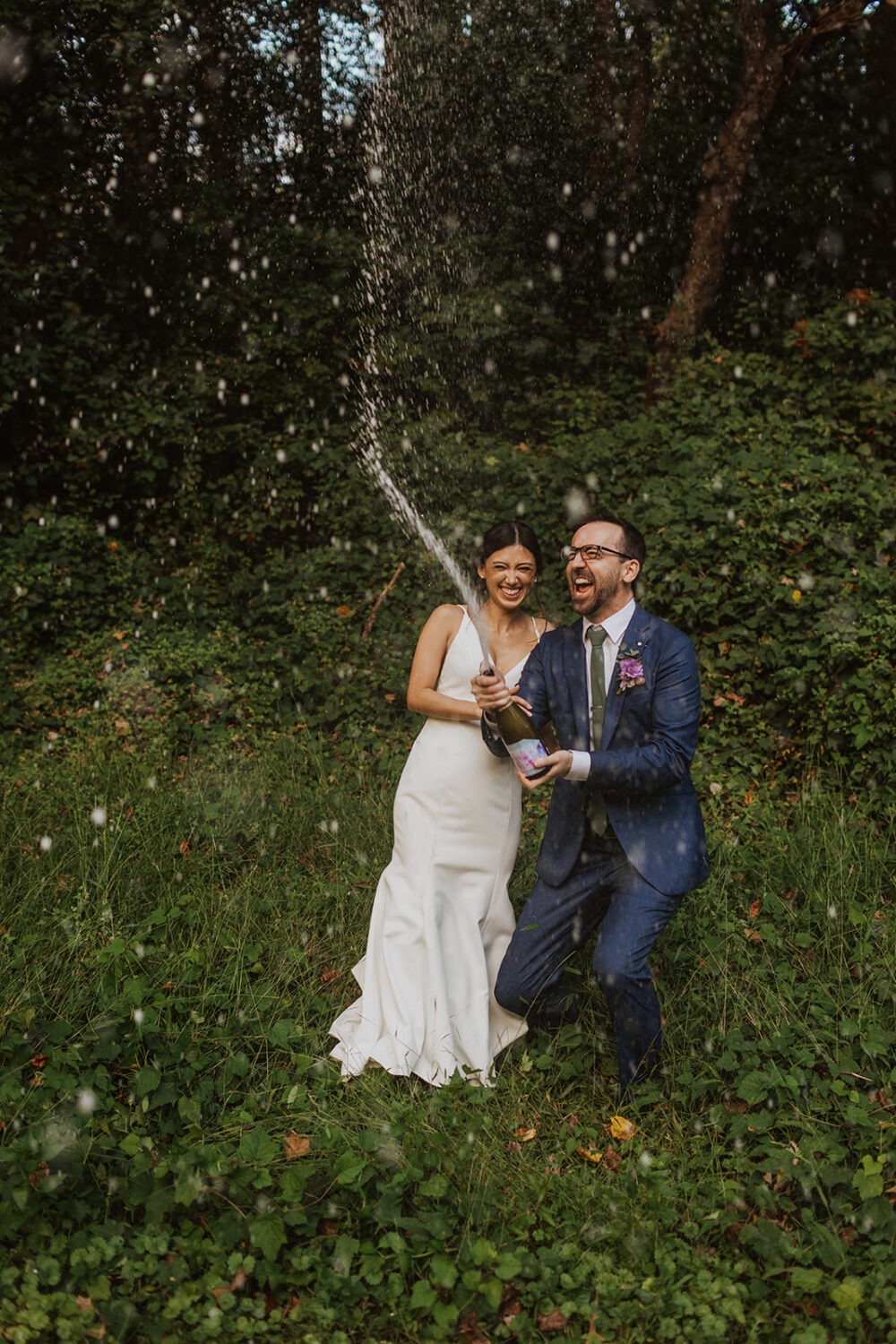 couple pops champagne at outdoor elopement