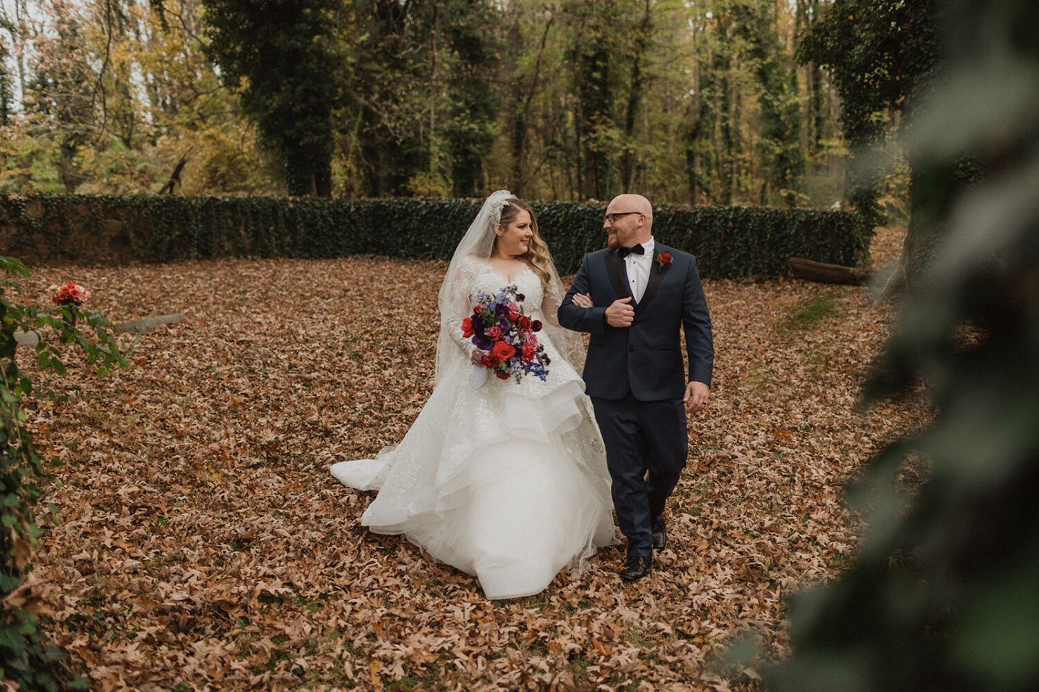 couple walks through forest at outdoor fall wedding venue