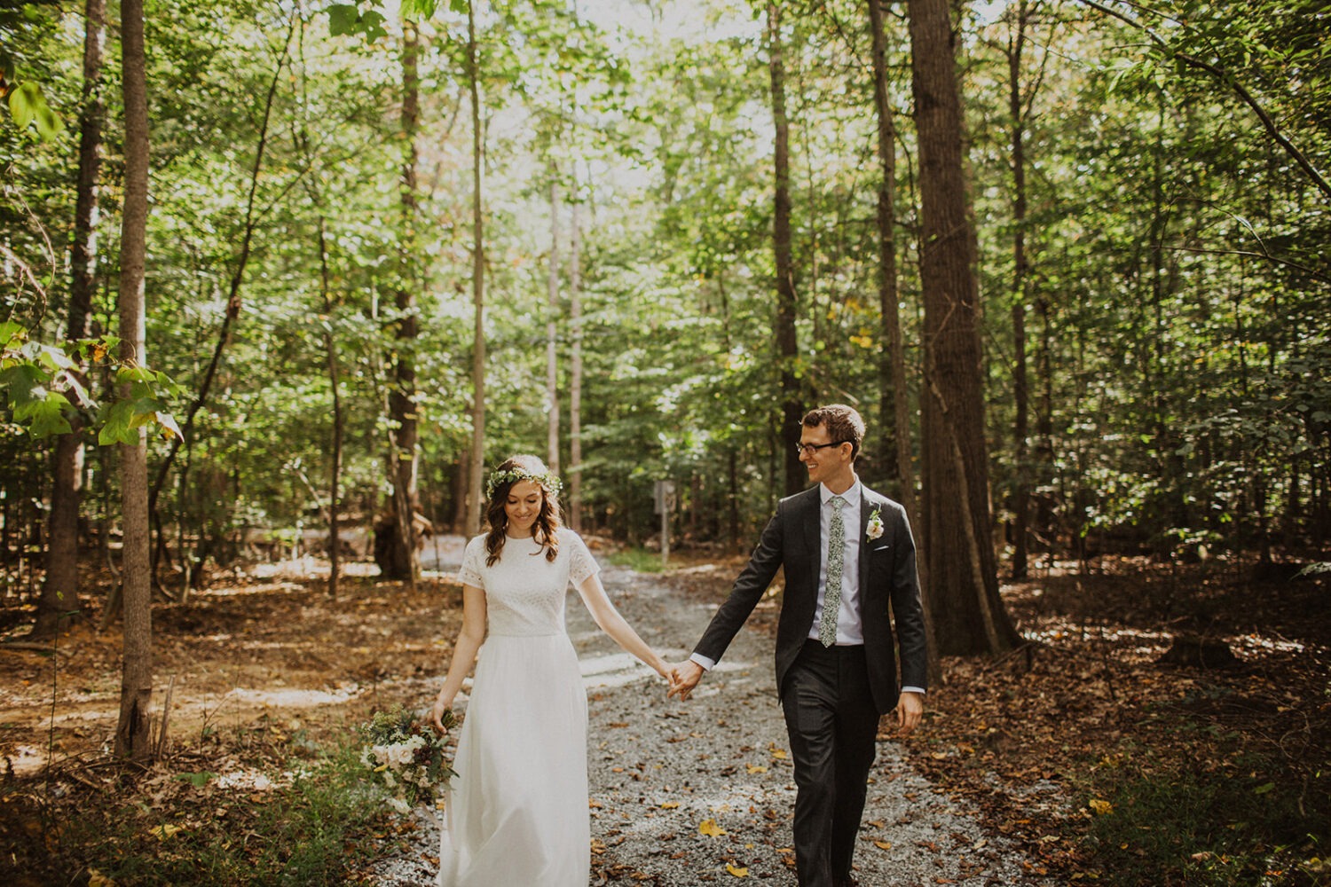 couple walks holding hands through woods at sunset Virginia elopement