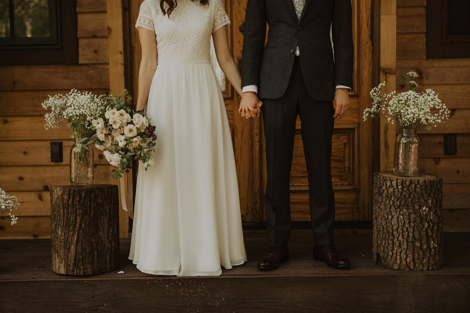couple stands holding hands in front of a-frame cabin wedding venue