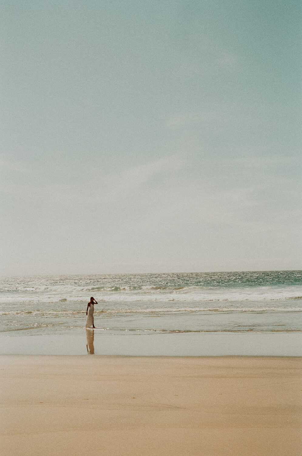 bride walks across beach in wedding film photography