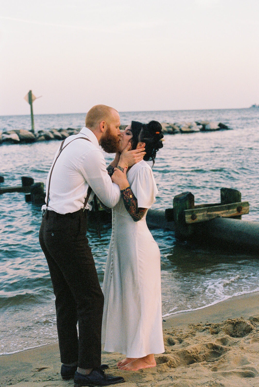 couple kisses along waterfront at beach wedding