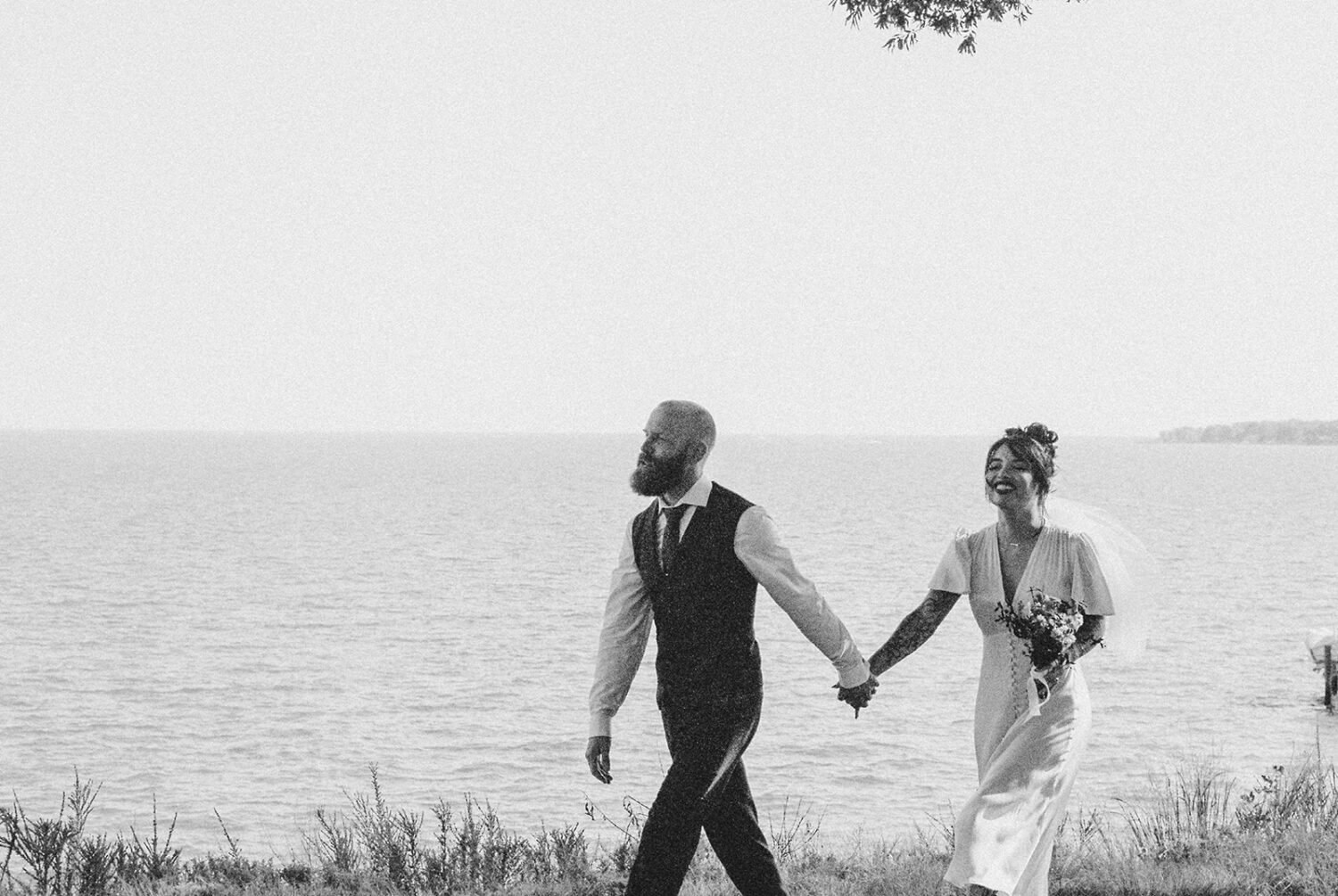 couple walks hand in hand along waterfront captured by film wedding photography