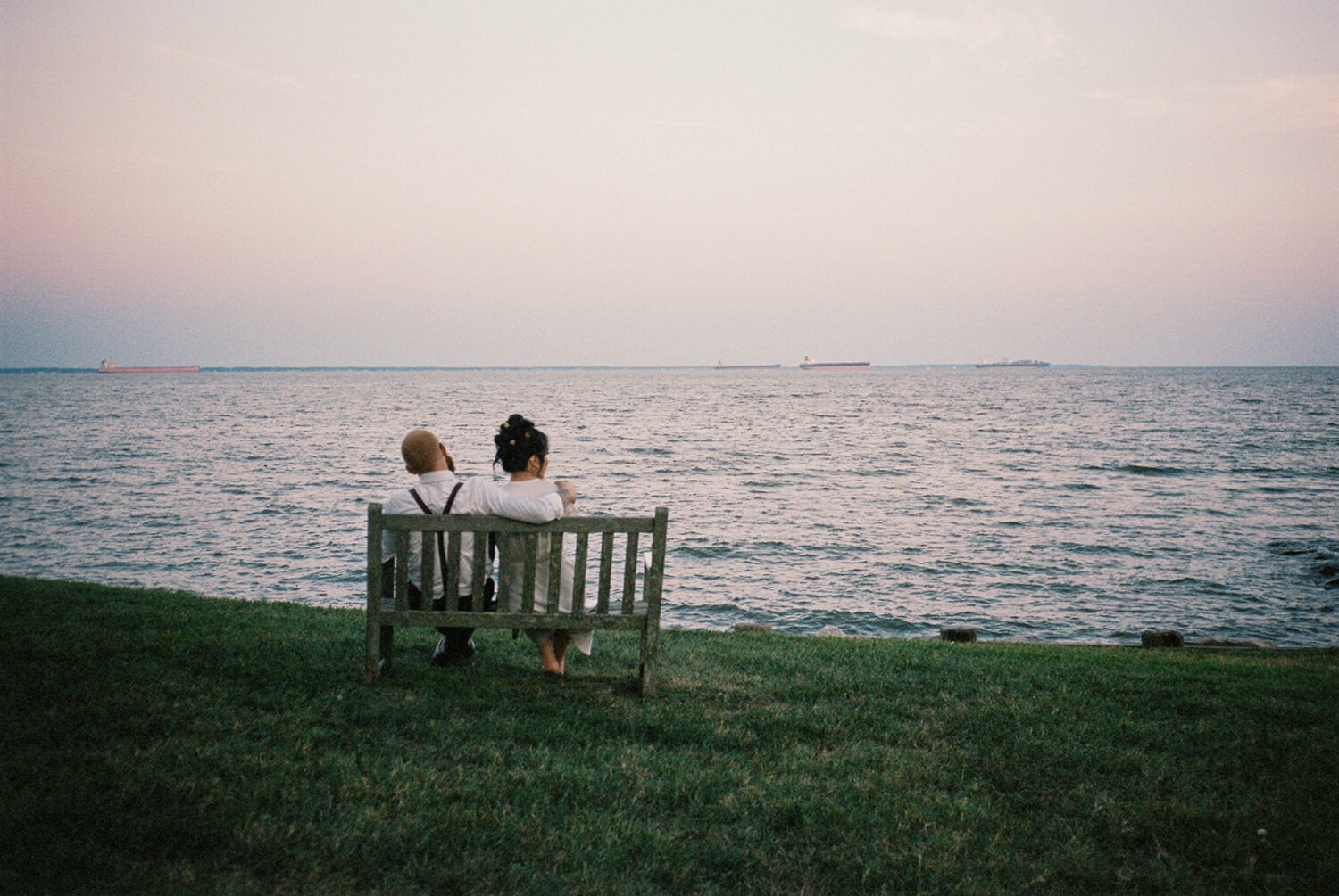 couple sits on bench watching sunset captured by film wedding photography