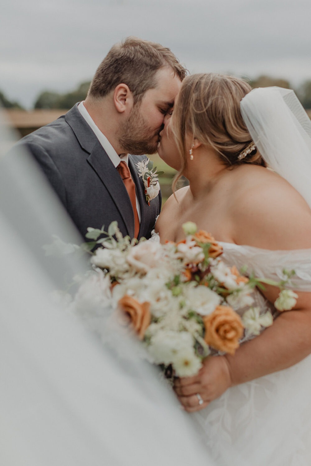 couple kisses under veil holding wedding bouquet 
