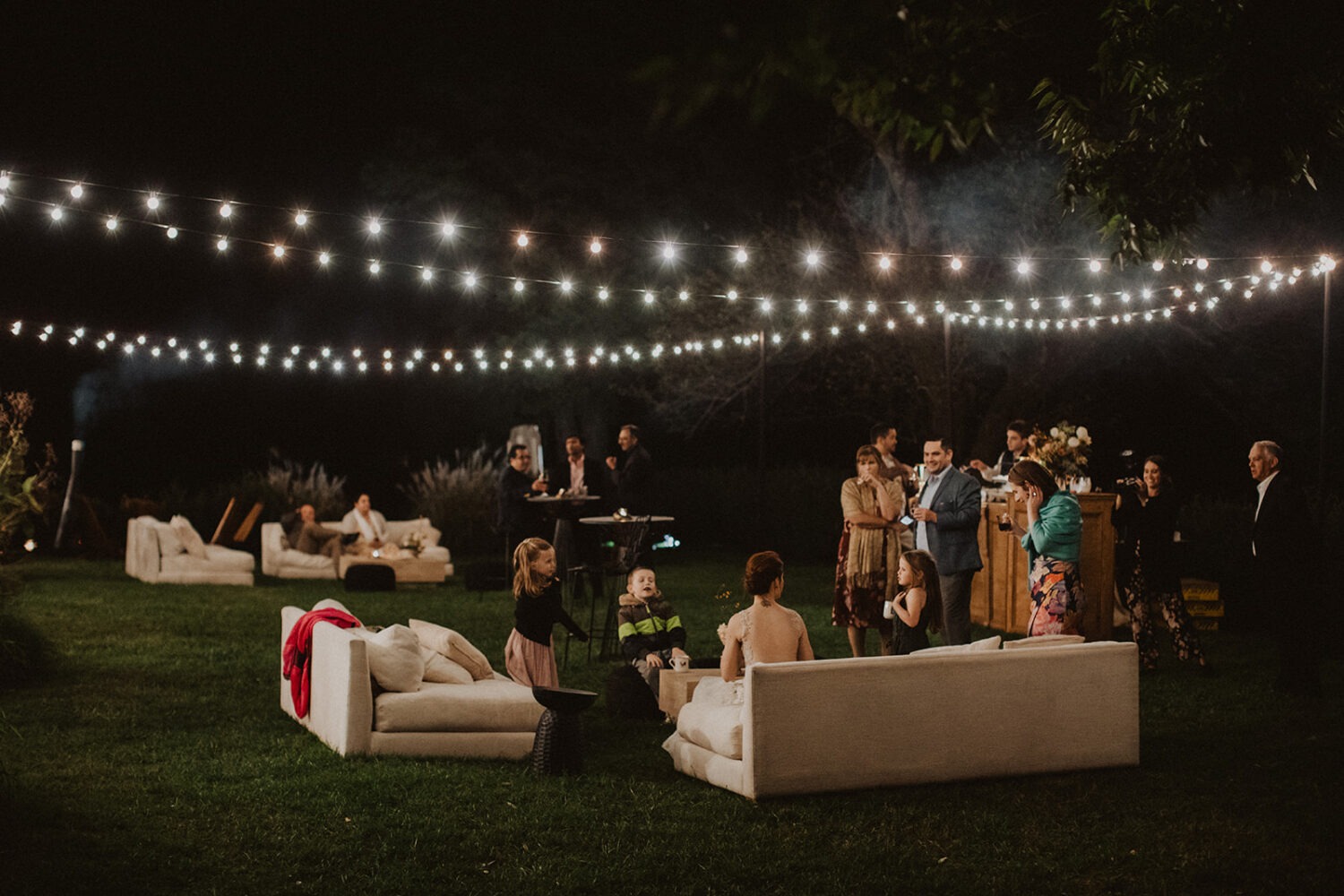 bride sits with guests under twinkle lights at outdoor Virginia wedding venue
